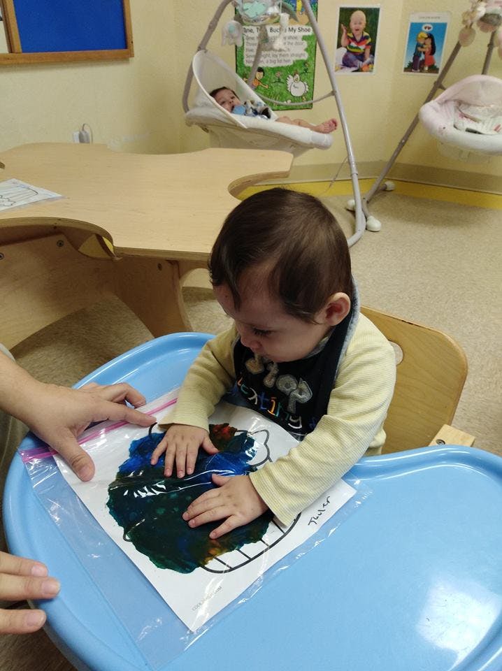 Child in a high chair playing with paint in a plastic bag