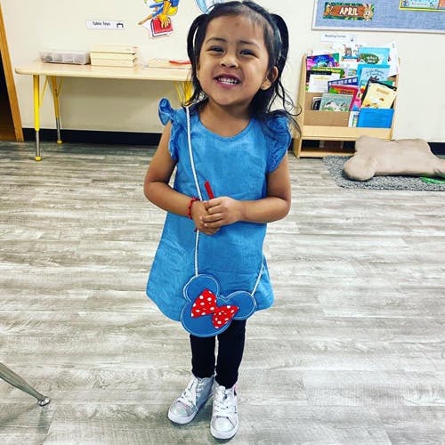 Child in a blue dress holding a Minnie Mouse purse