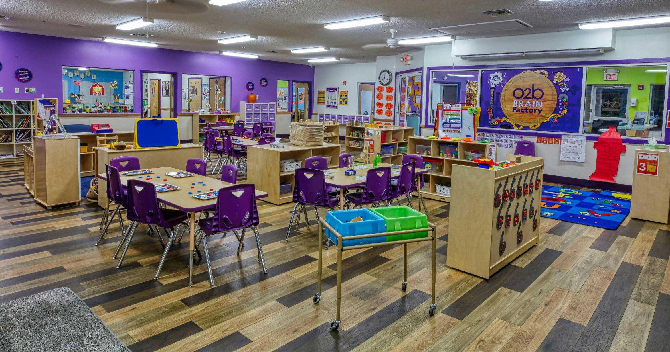 Classroom with purple walls, tables with purple chairs, and toys