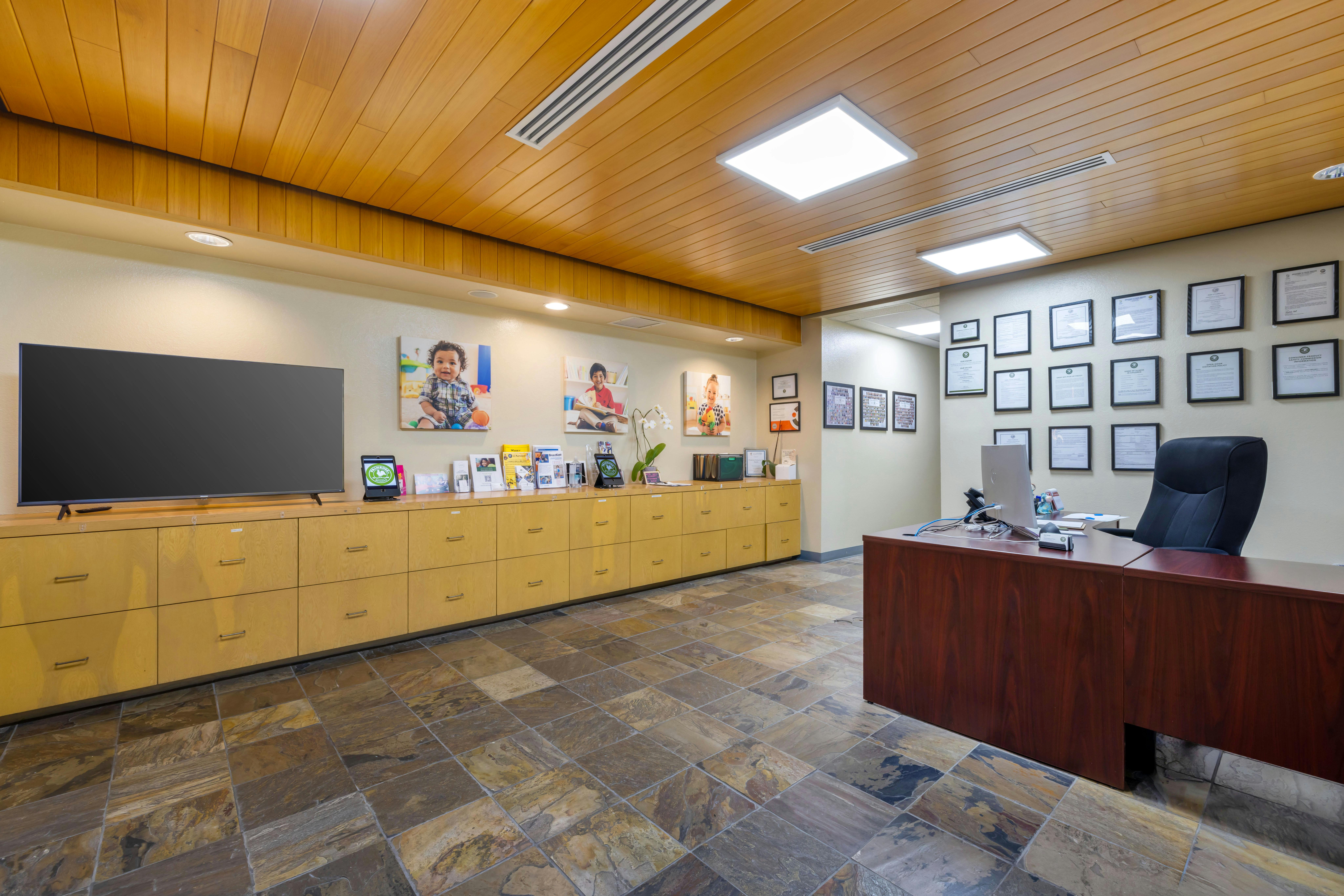 Reception area with a wooden ceiling and light-colored file cabinets, a large TV, and a desk