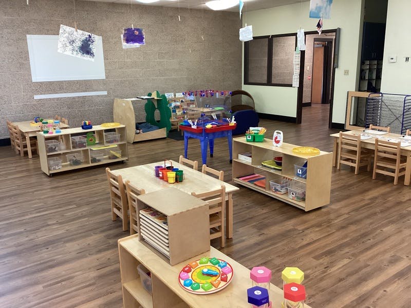 Empty classroom with small tables, chairs, and shelves