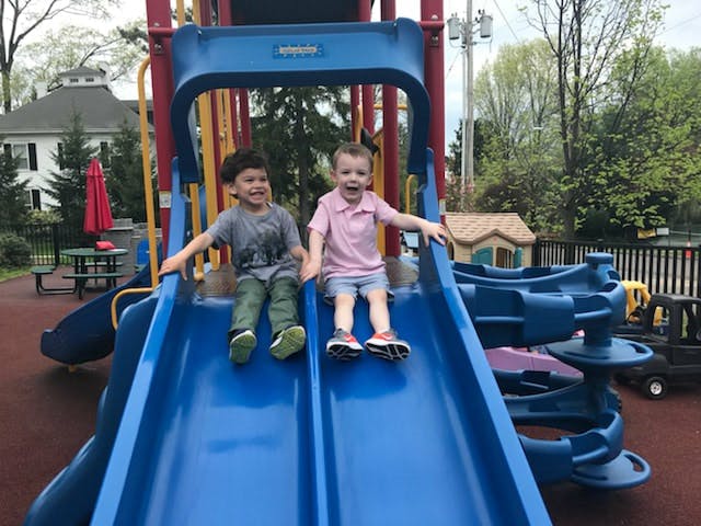 Two children sitting at the top of a blue playground slide