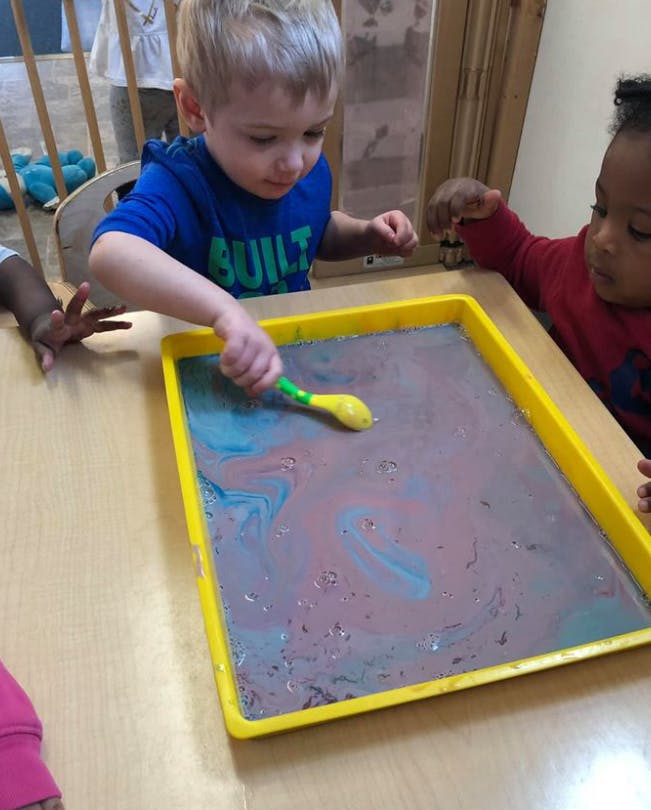 Child stirring liquid in a yellow tray with a spoon