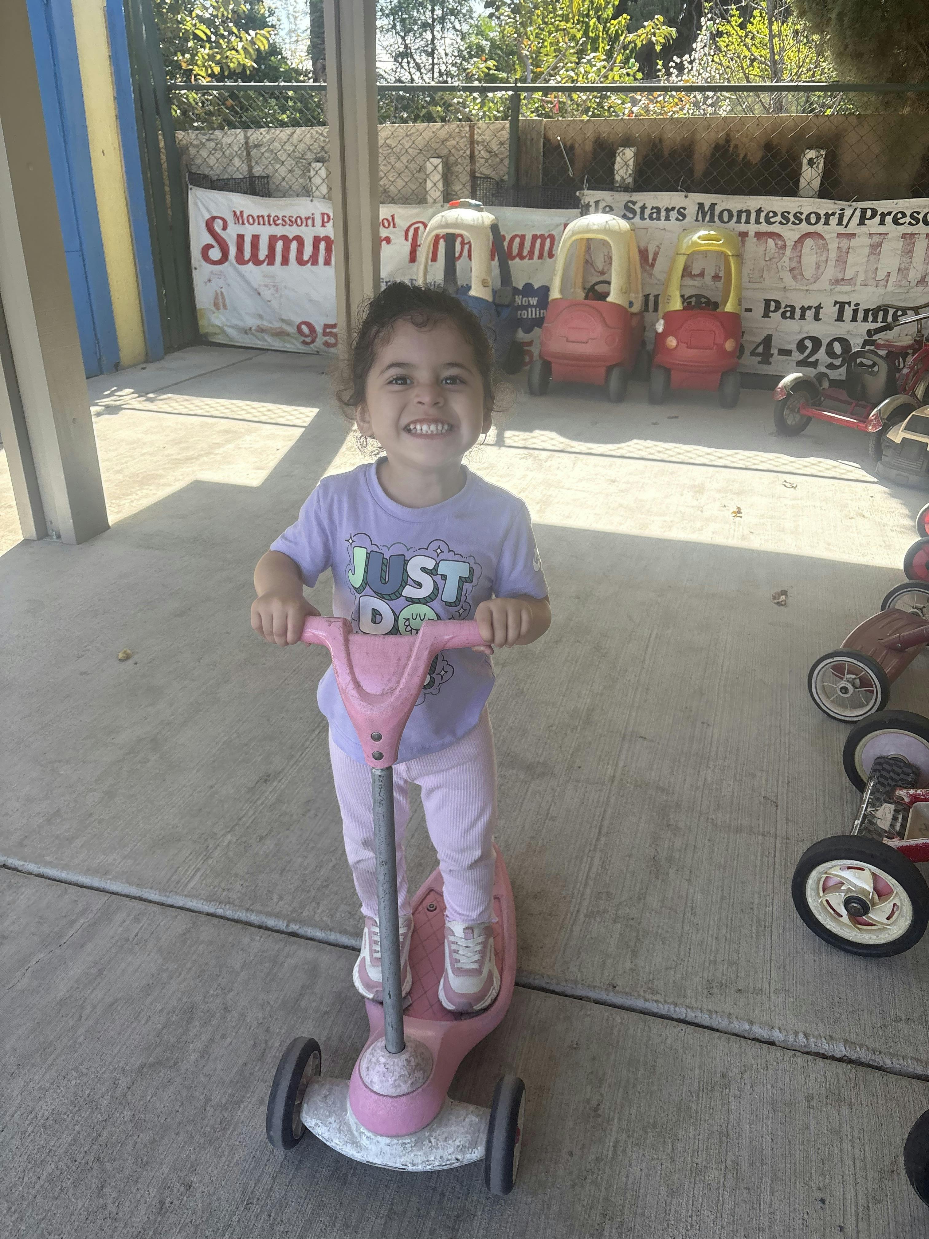 Child standing on a pink toy scooter at a preschool