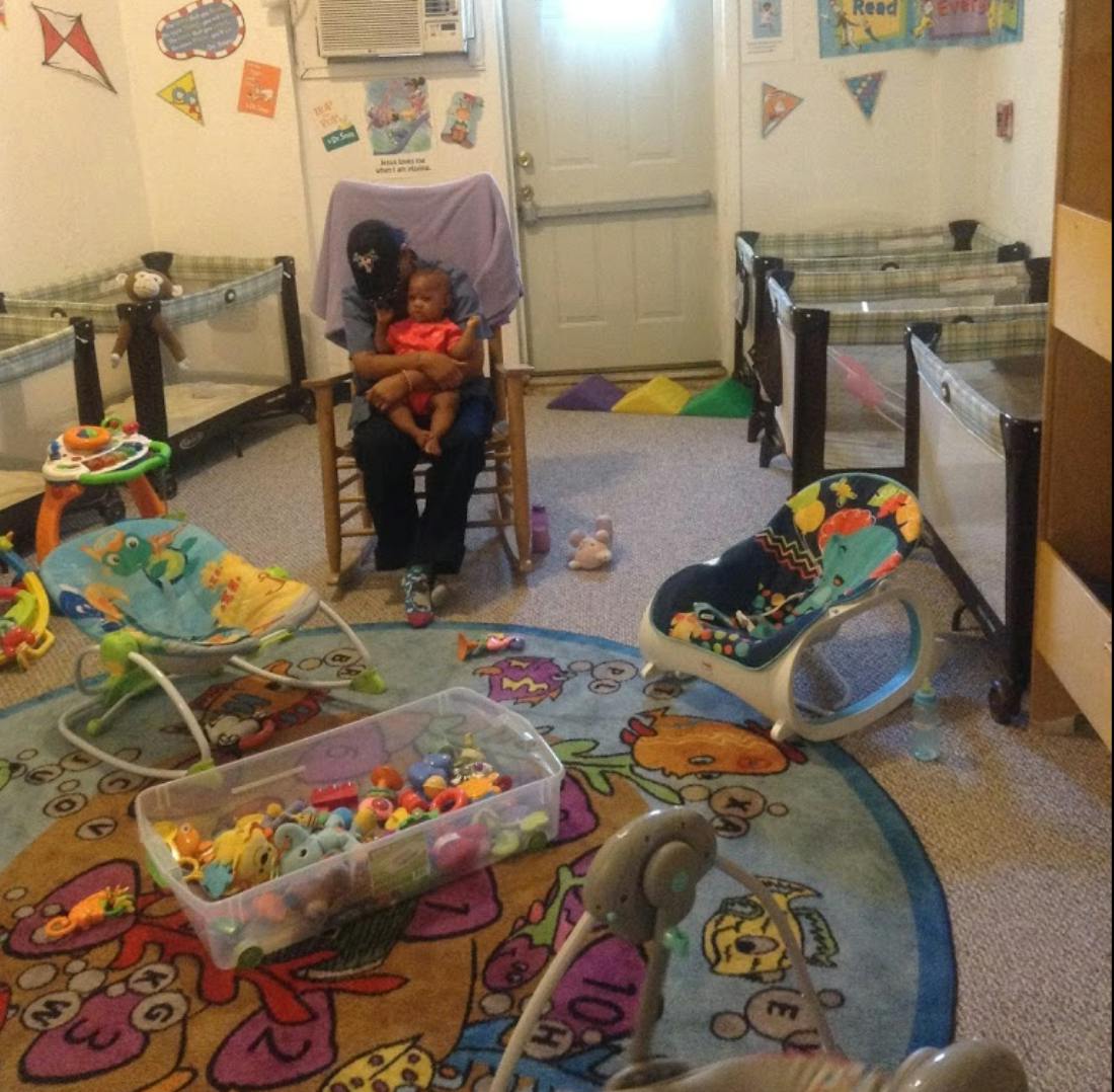 Person holding a child in a rocking chair in a room with cribs and toys
