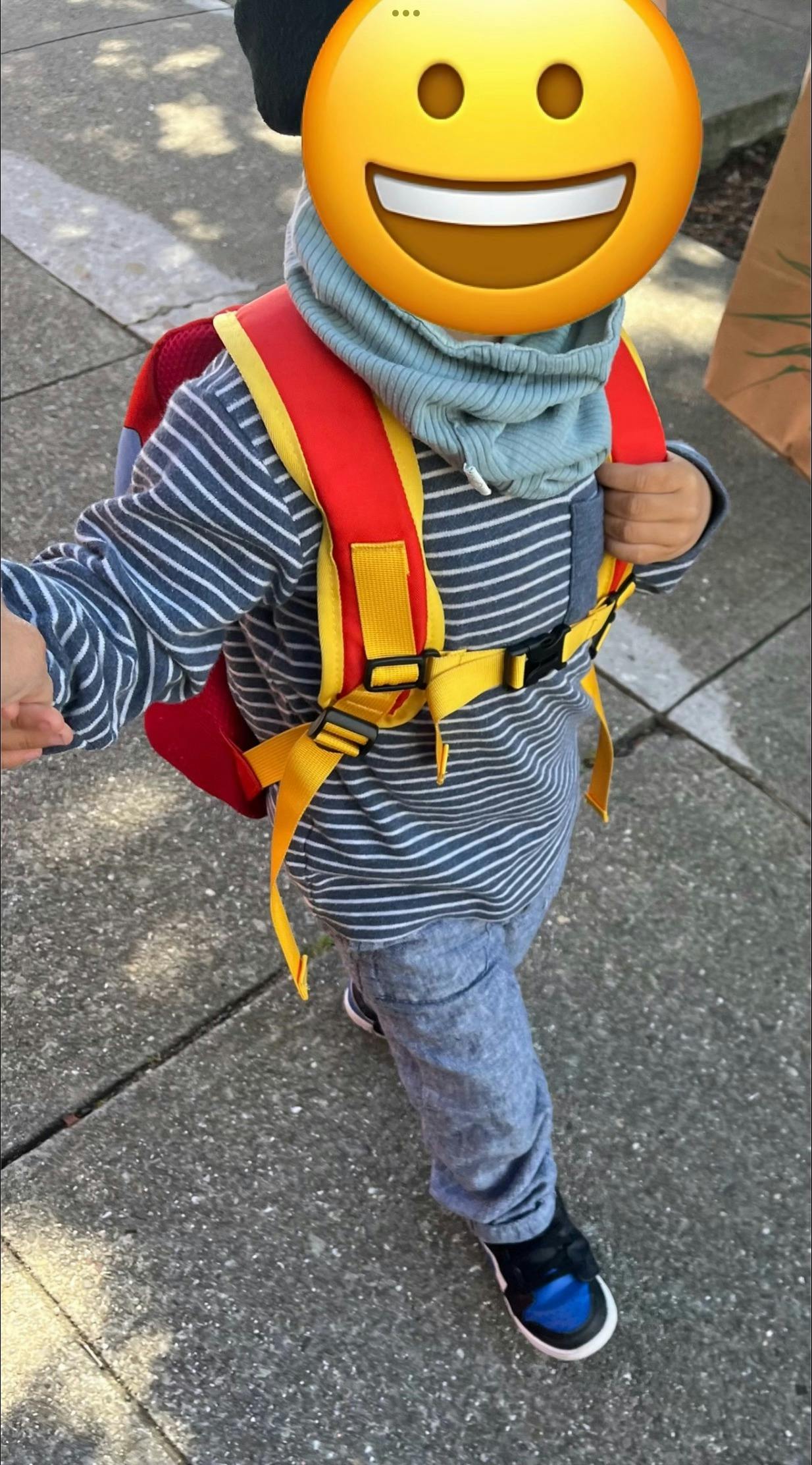Child wearing a red and yellow backpack and a blue scarf
