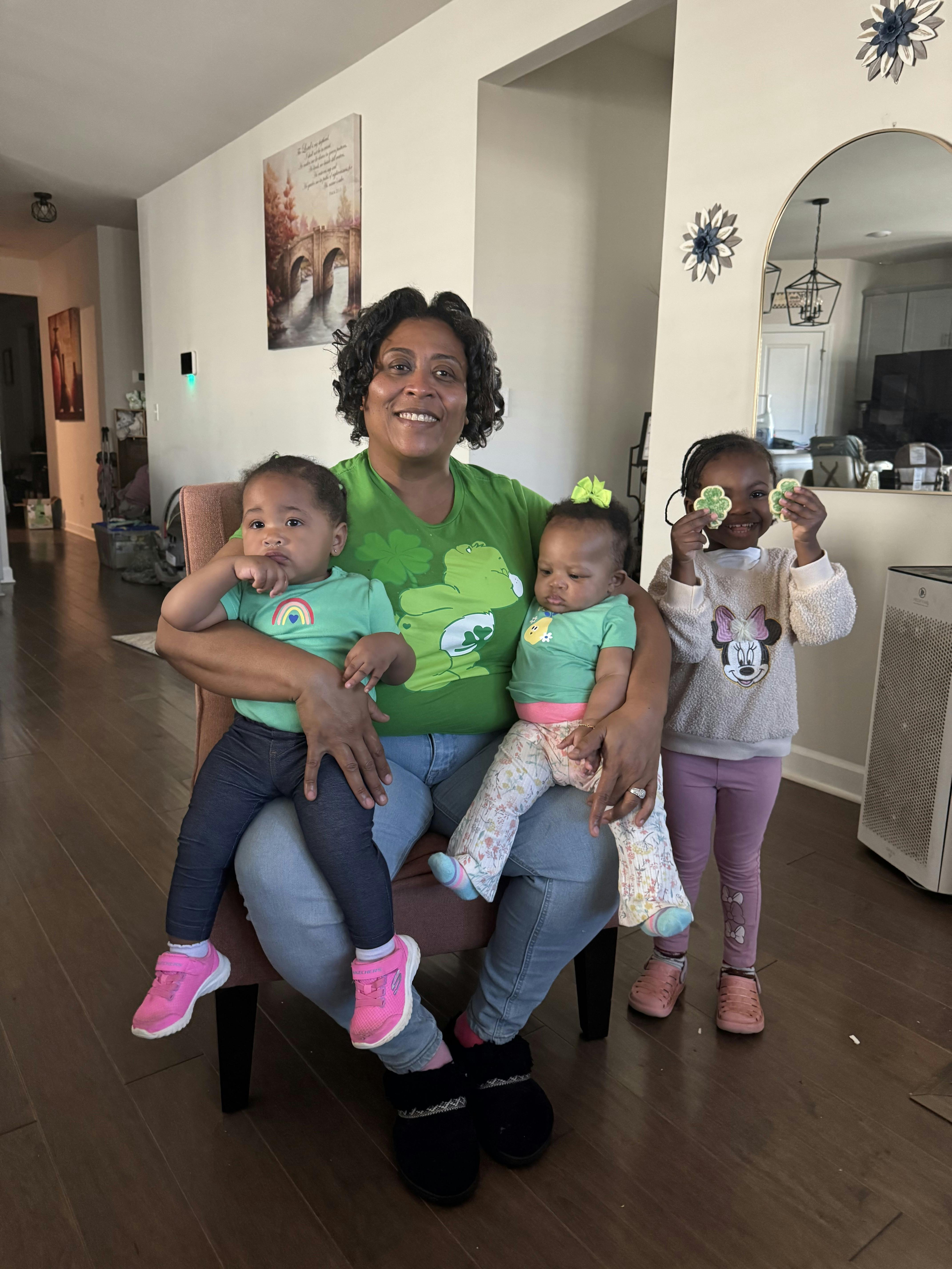 Person holding two infants on their lap, child standing next to them holding shamrocks