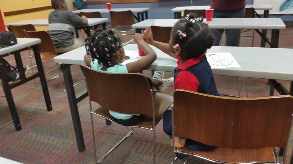 Two children sitting at a table, one reaching out to the other