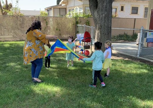Adult and children playing with a colorful parachute on grass