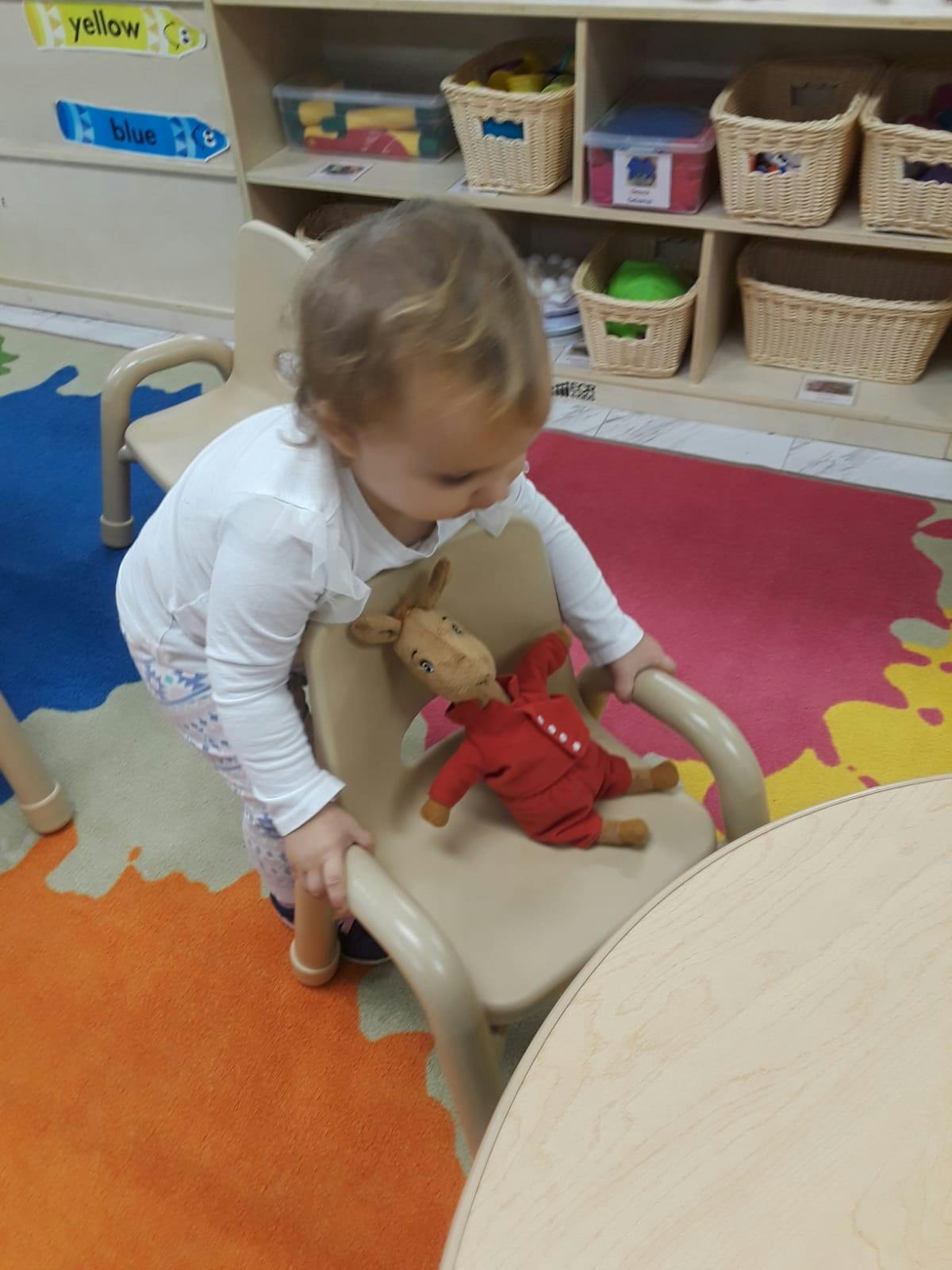 Child standing next to a chair with a stuffed animal on it