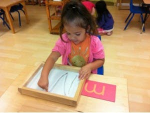 Child tracing in a sand tray with a letter card next to it