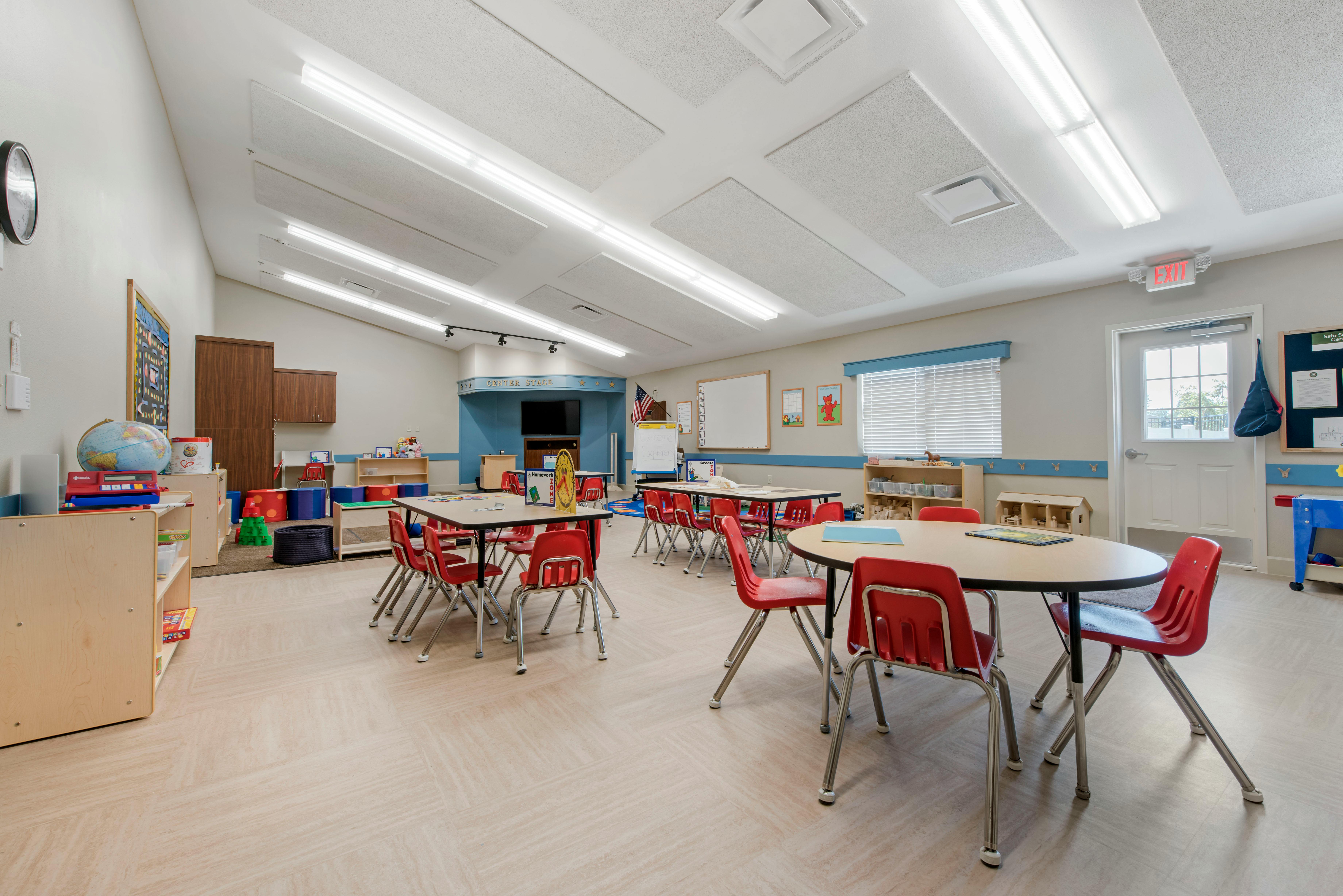 An empty classroom with several tables and red chairs, and a small stage