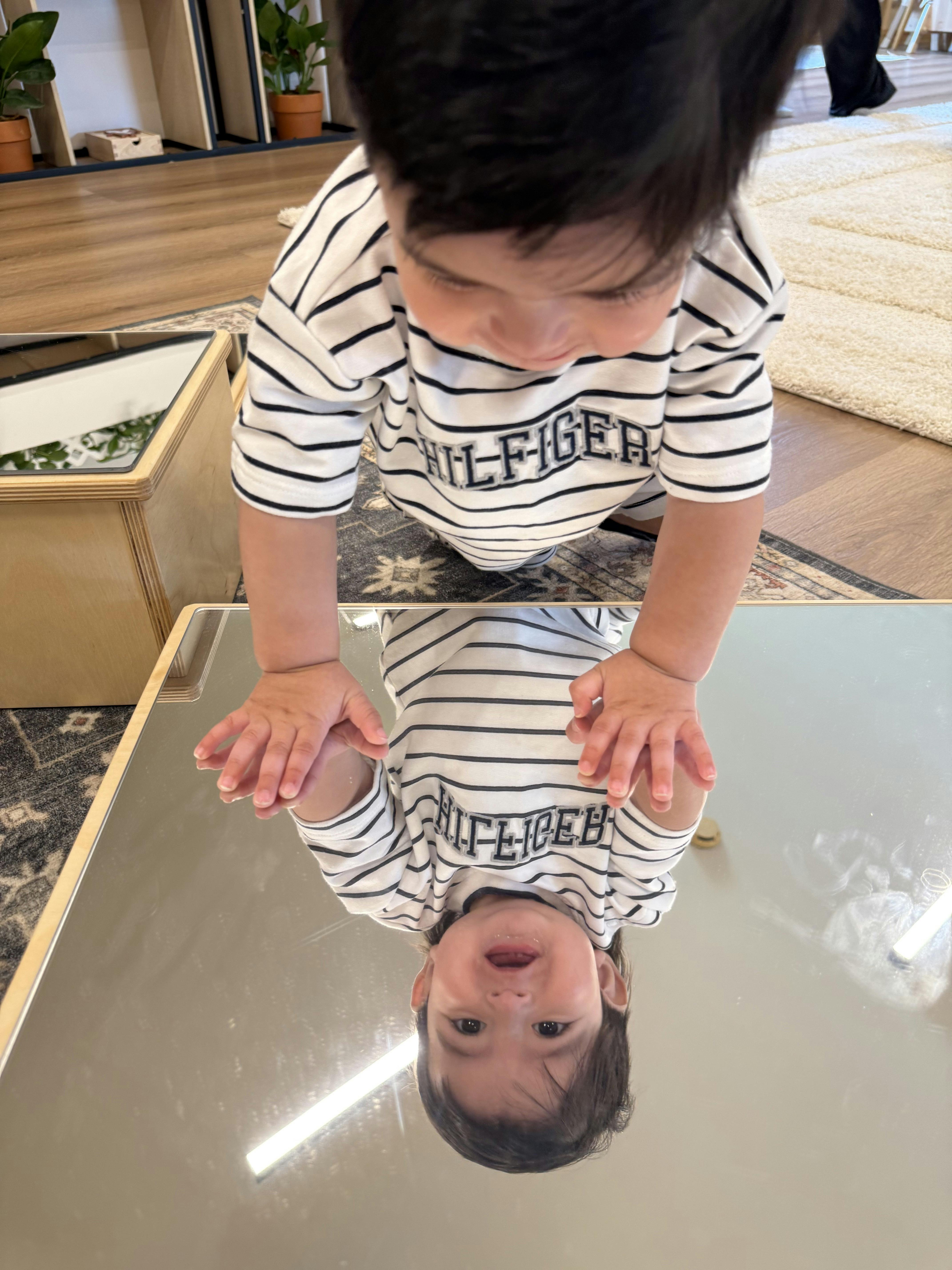 Child in a striped shirt looking at their reflection in a floor mirror