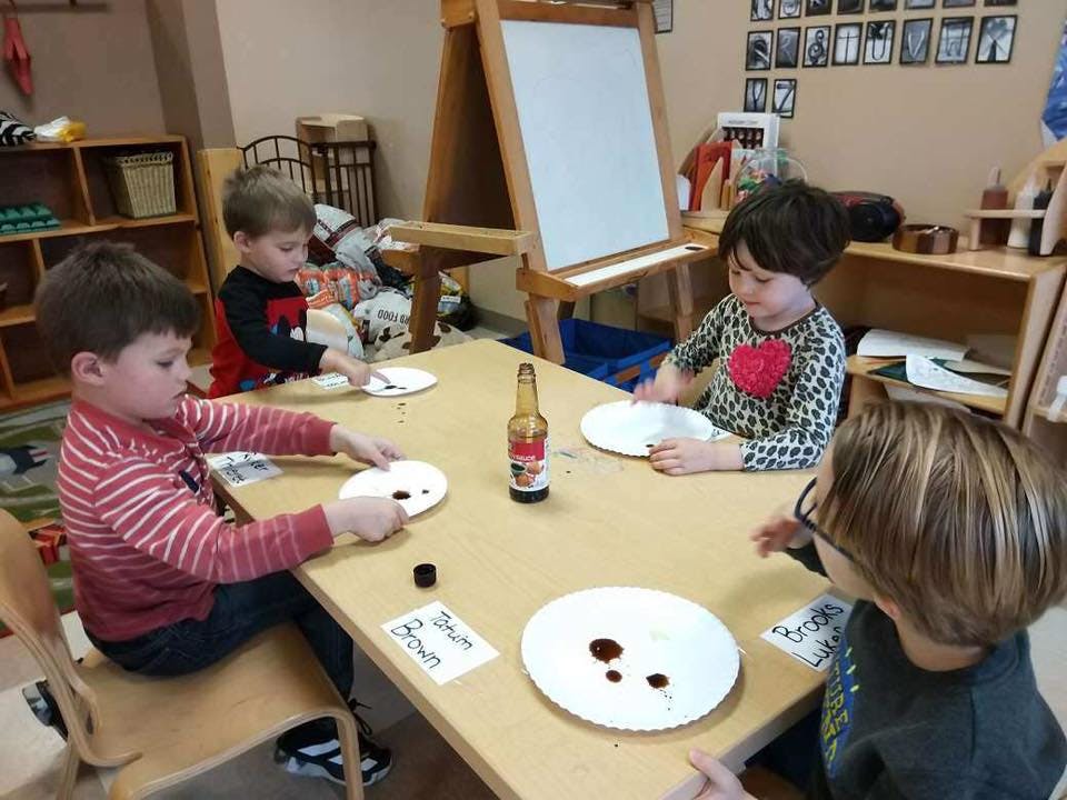 Four children sitting at a table doing an art activity with paint on paper plates