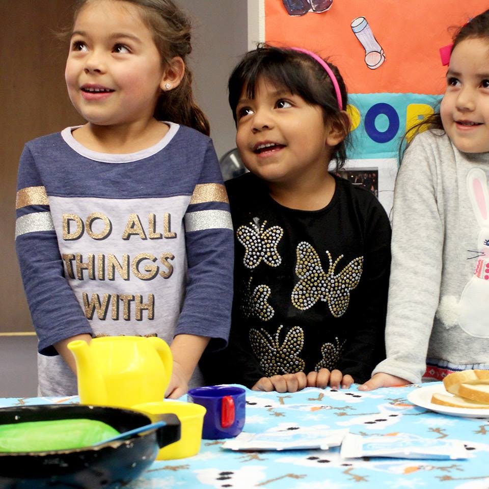 Three children looking up, with play dishes on a table in front