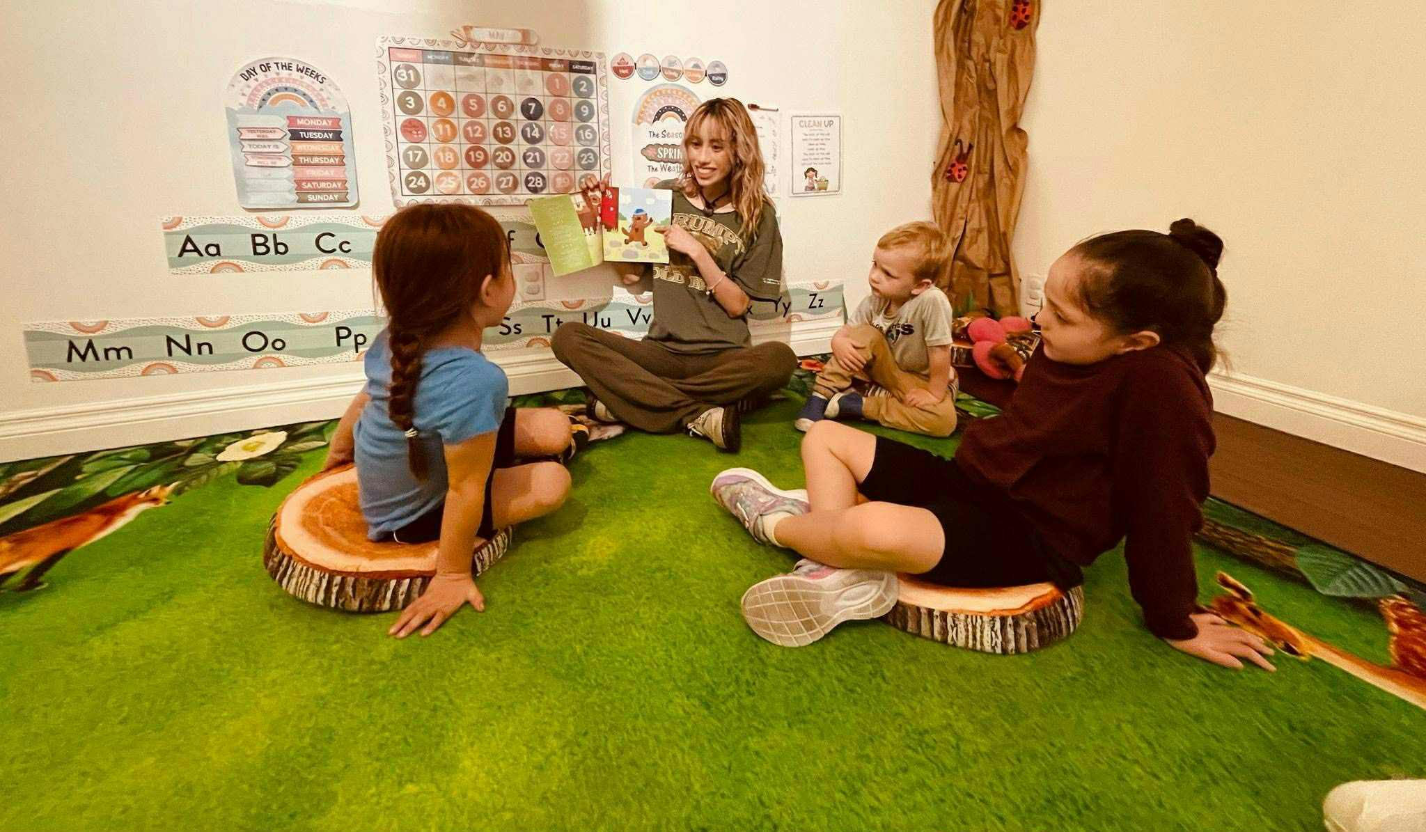 A person reading a book to three children in a classroom