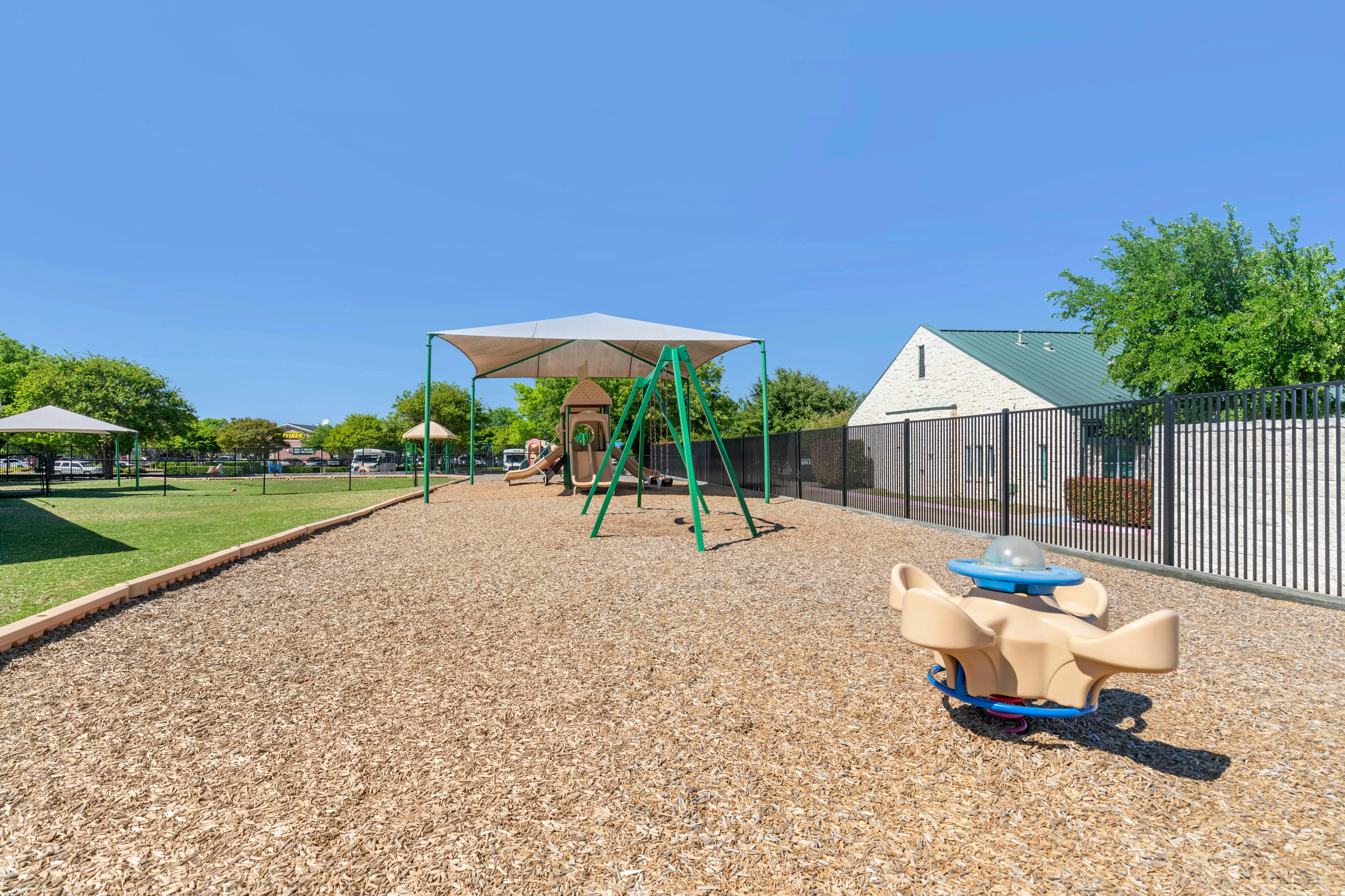 Playground area with wood chips, covered play structure, swings, and a spring rider