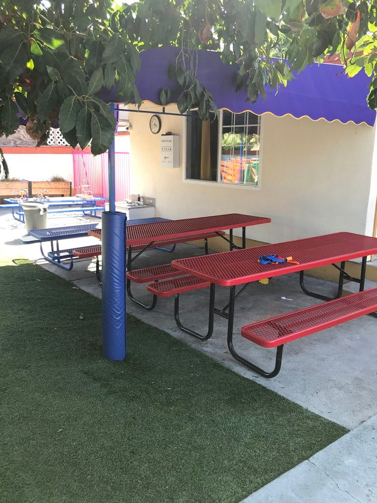Red picnic tables under a purple awning next to a building