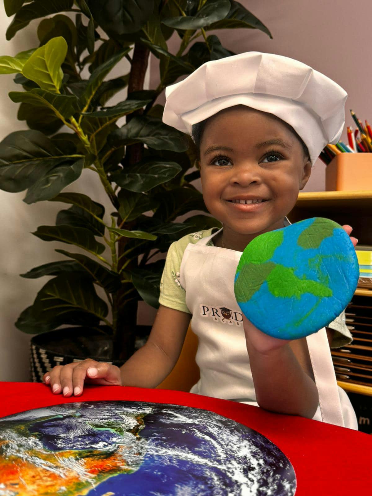Child in chef hat and apron holding a painted earth