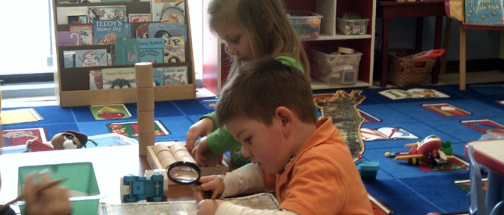 Child looking through a magnifying glass, another child in background