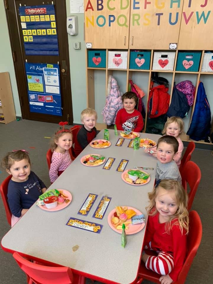 Children sitting at a table with plates of food in a classroom