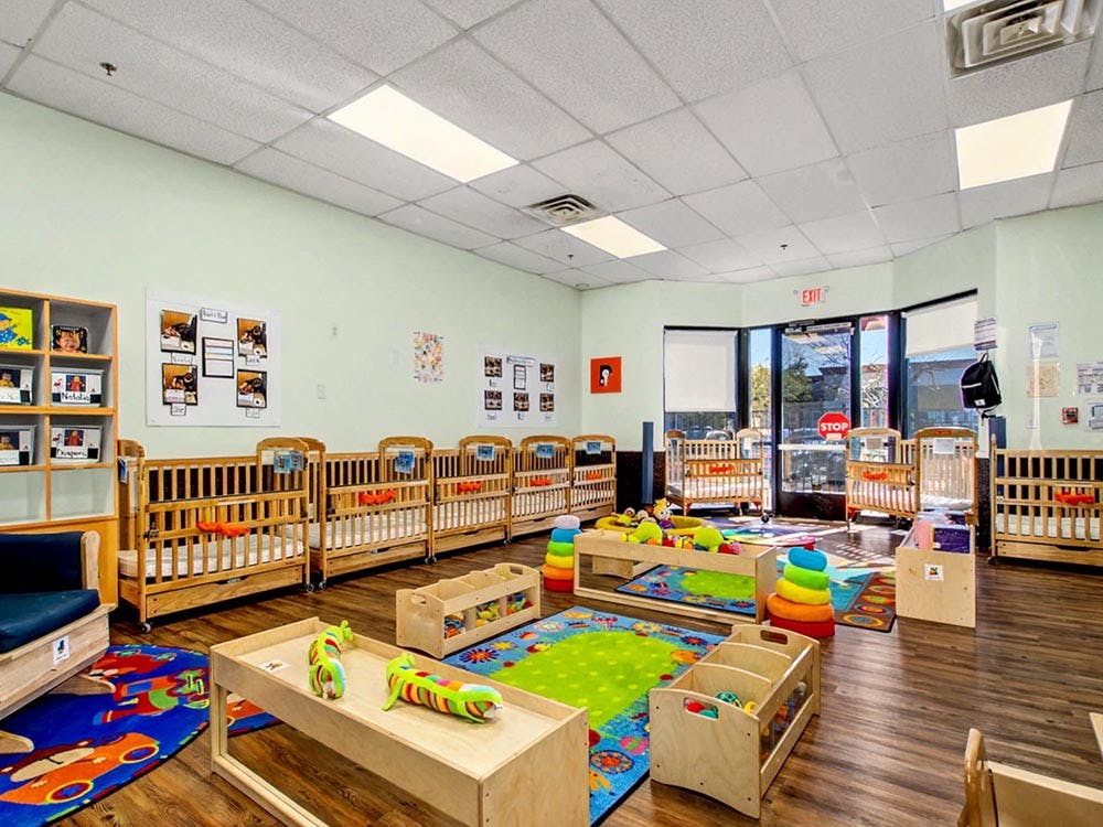 A room with multiple wooden cribs, colorful rugs, and play tables with toys