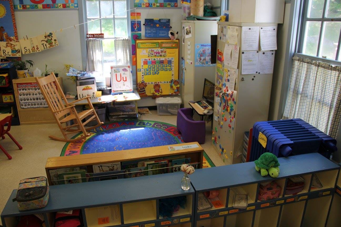 Classroom with a rocking chair, blue rug, and storage shelves