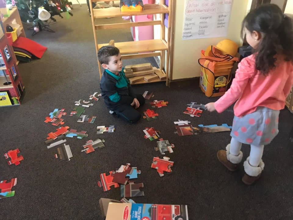 Two children playing with puzzle pieces on the floor
