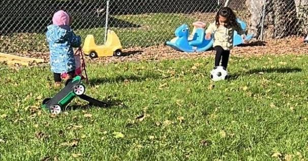 Two children playing with toys and a soccer ball in a grassy yard