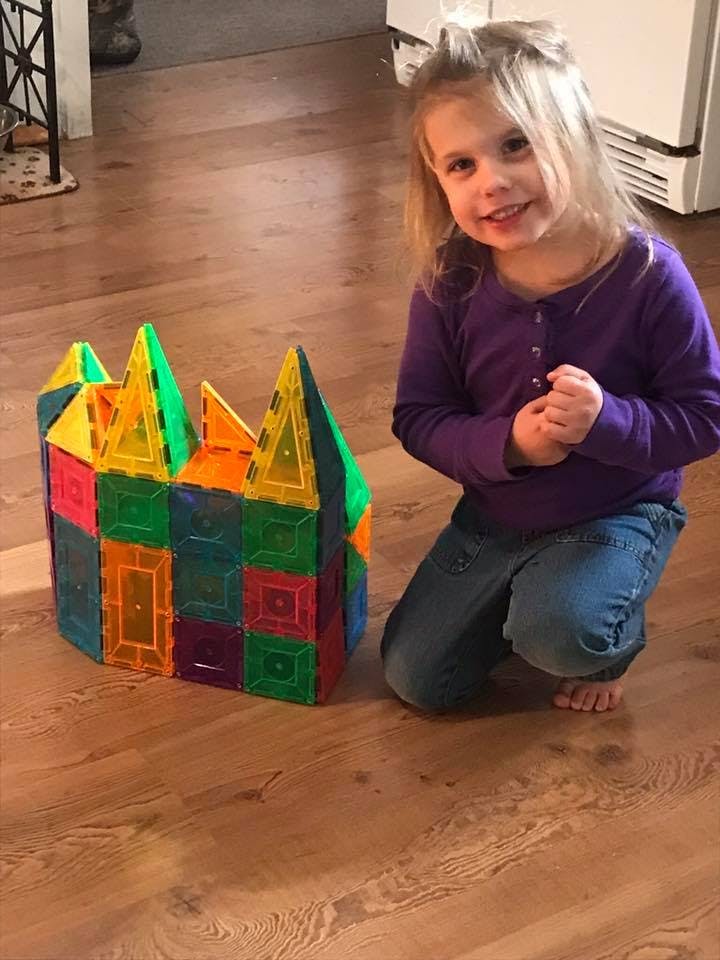 Child kneeling next to a colorful magnetic block structure