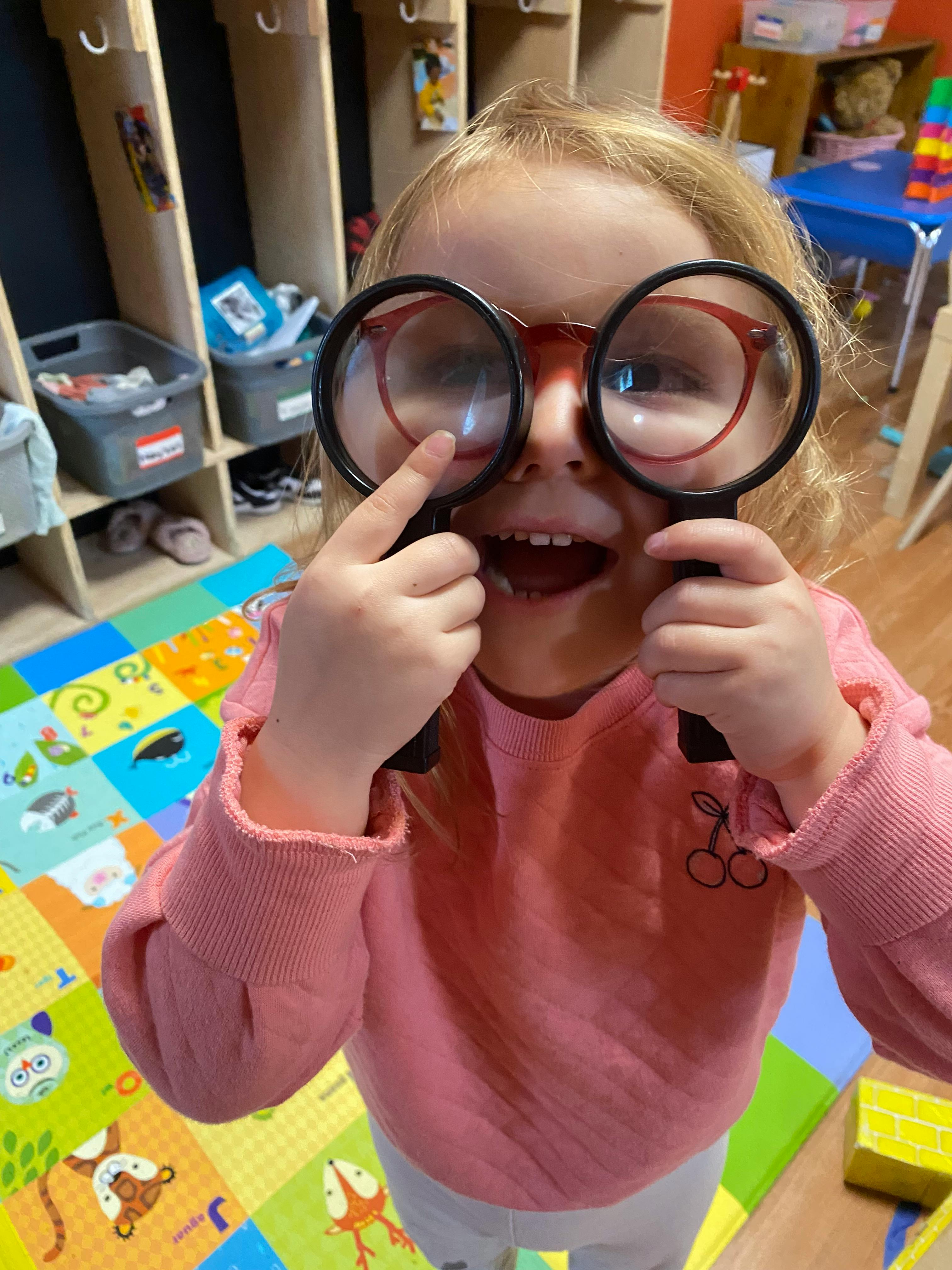 Child holding two large magnifying glasses over eyes