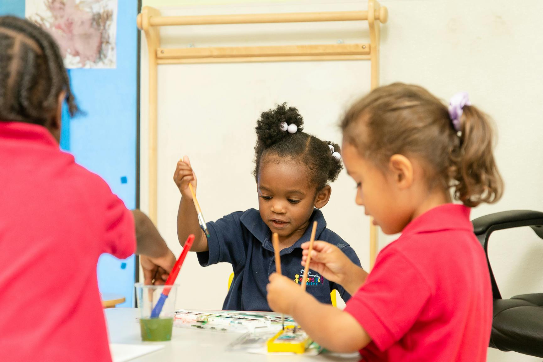 Three children painting in a classroom