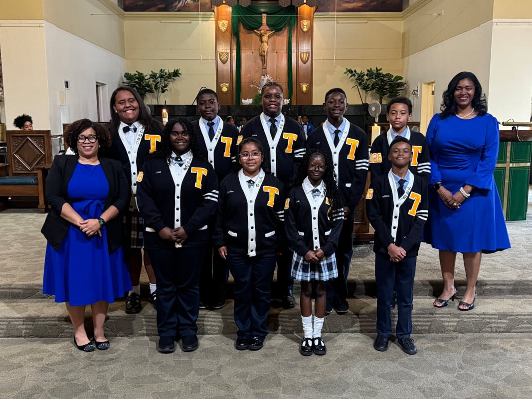 Two people standing with nine children and teens in matching cardigans in a church
