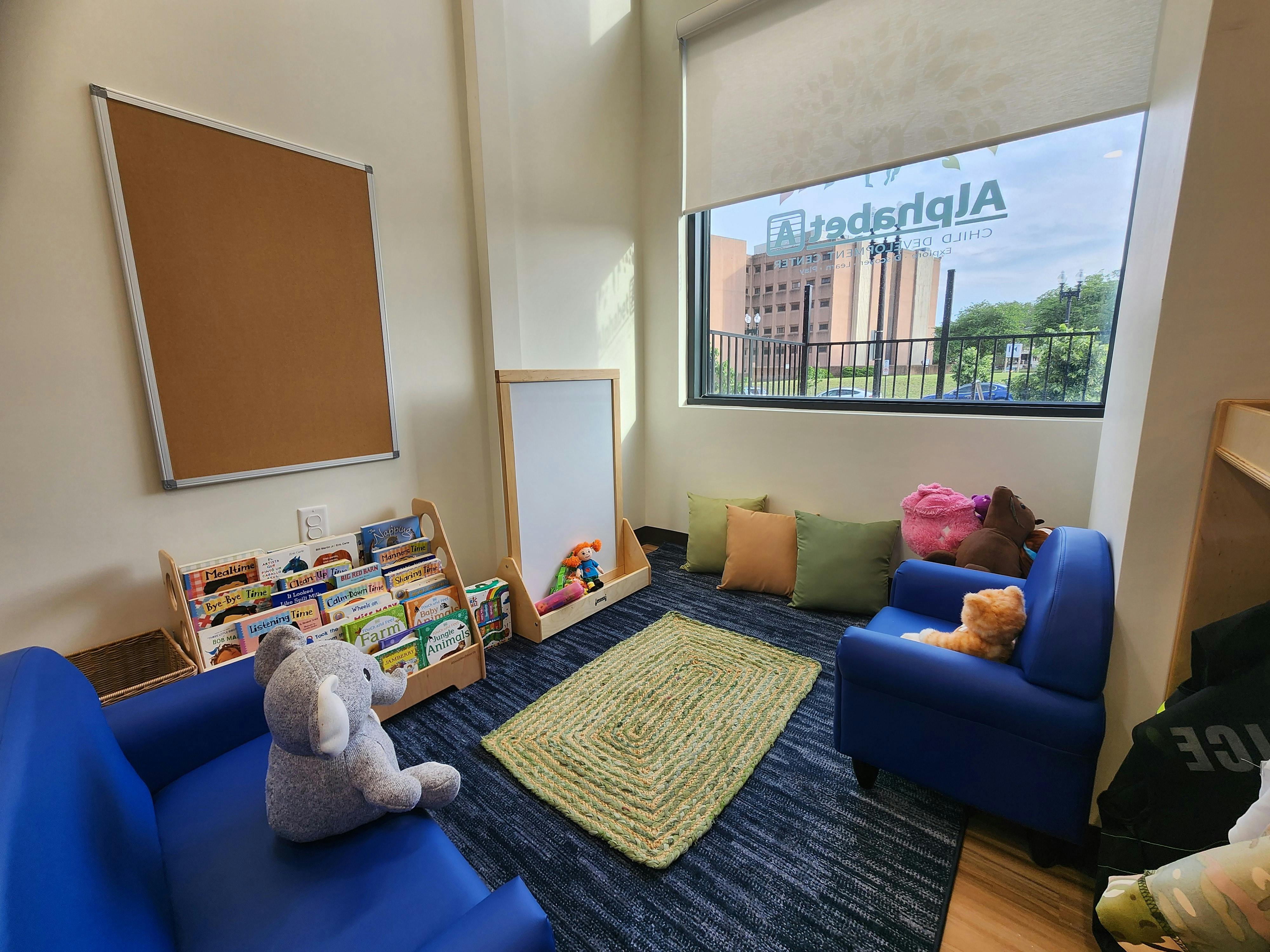 Children's reading nook with two blue chairs, books, and cushions by a window
