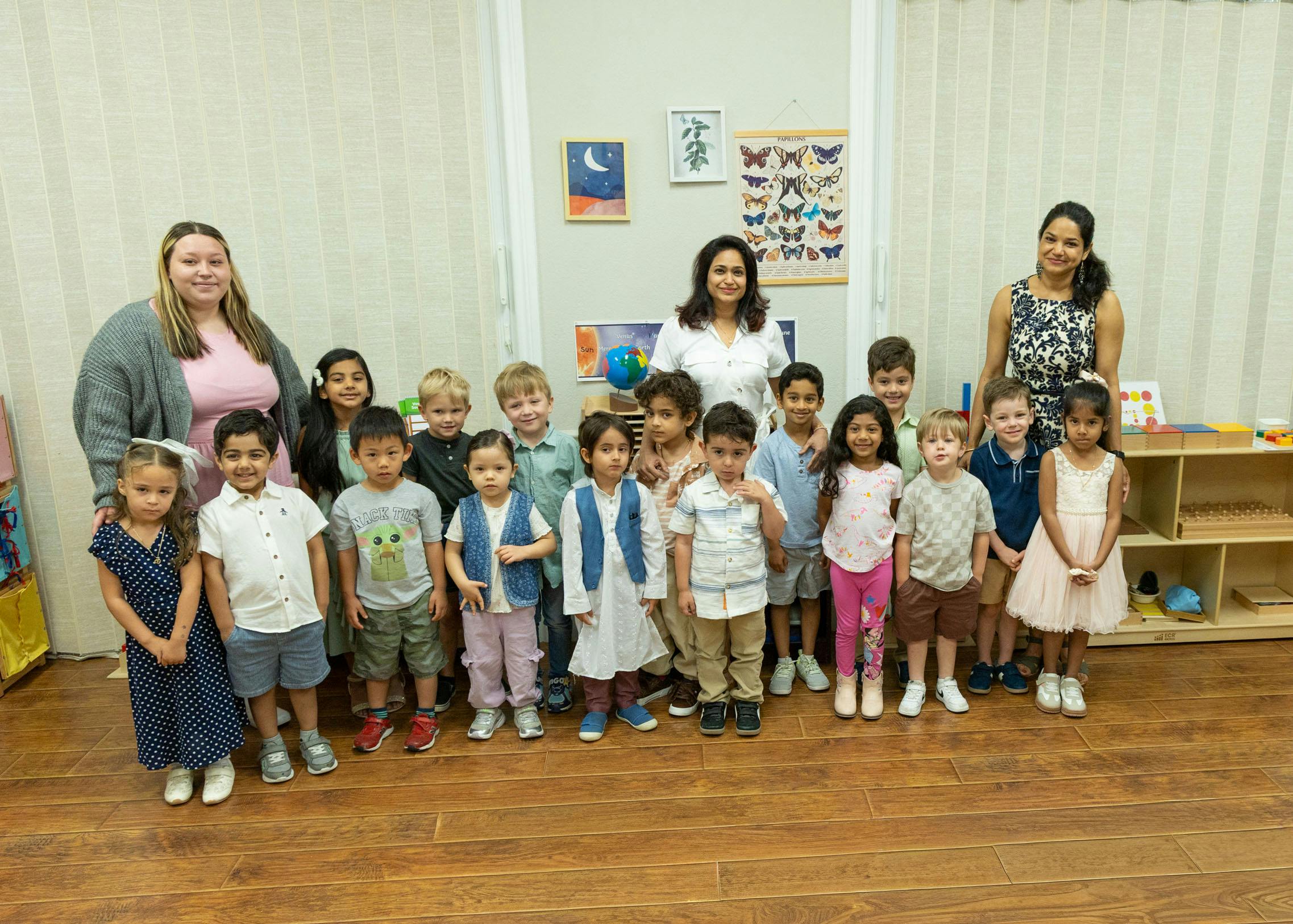 Group of three adults and many children standing in a classroom