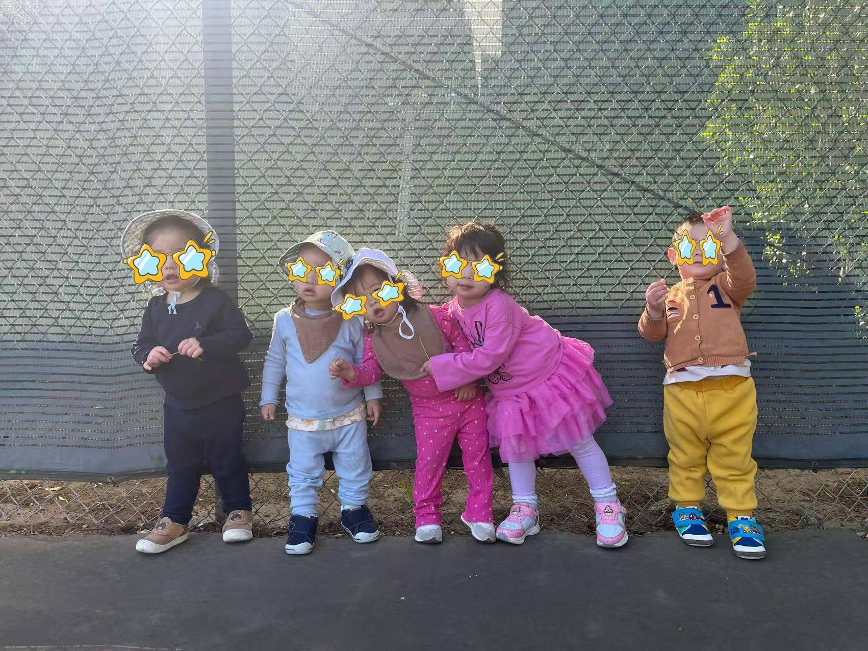 Five children standing in front of a green fence