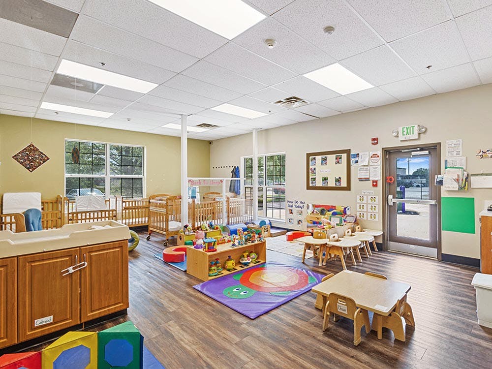 Classroom with cribs, small tables, and toys on the floor