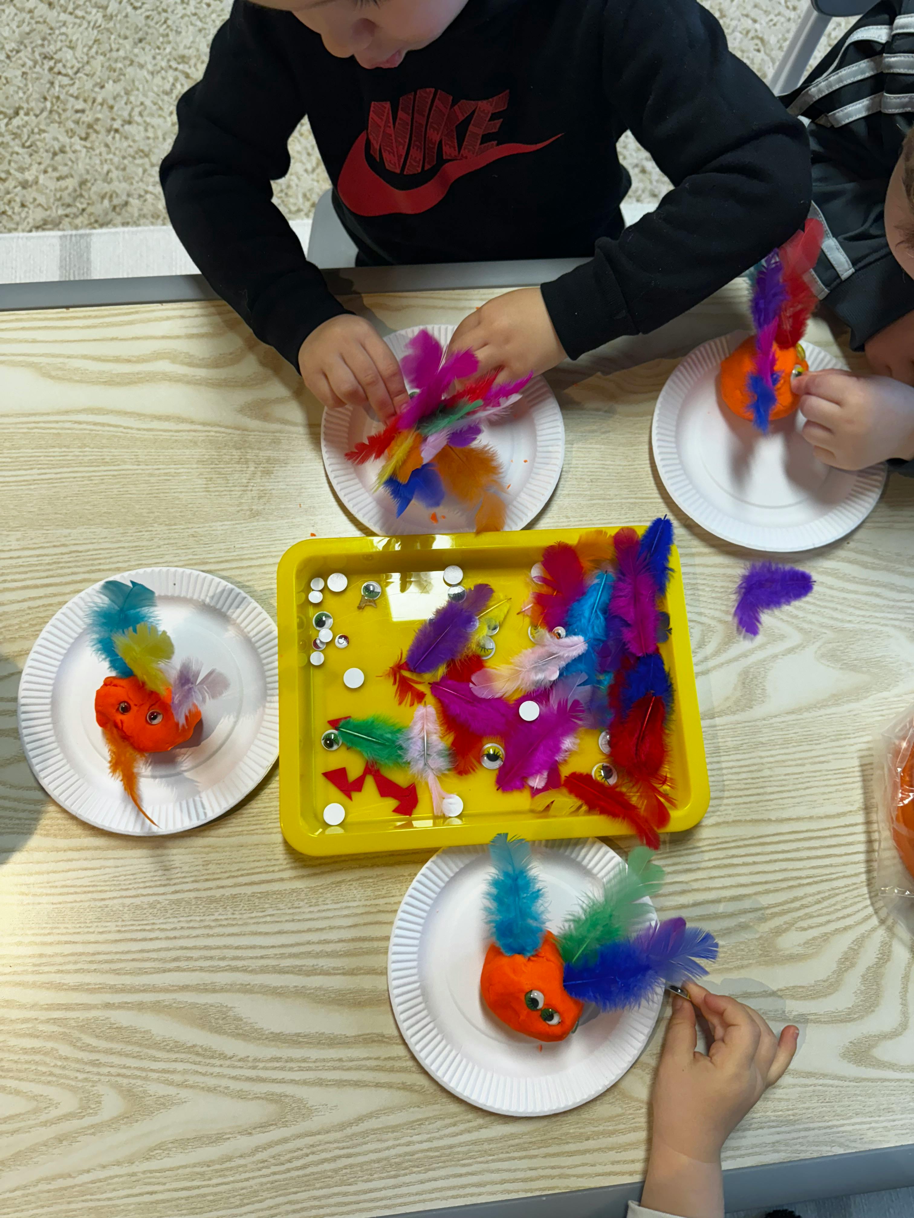 Children making crafts with colorful feathers and orange shapes
