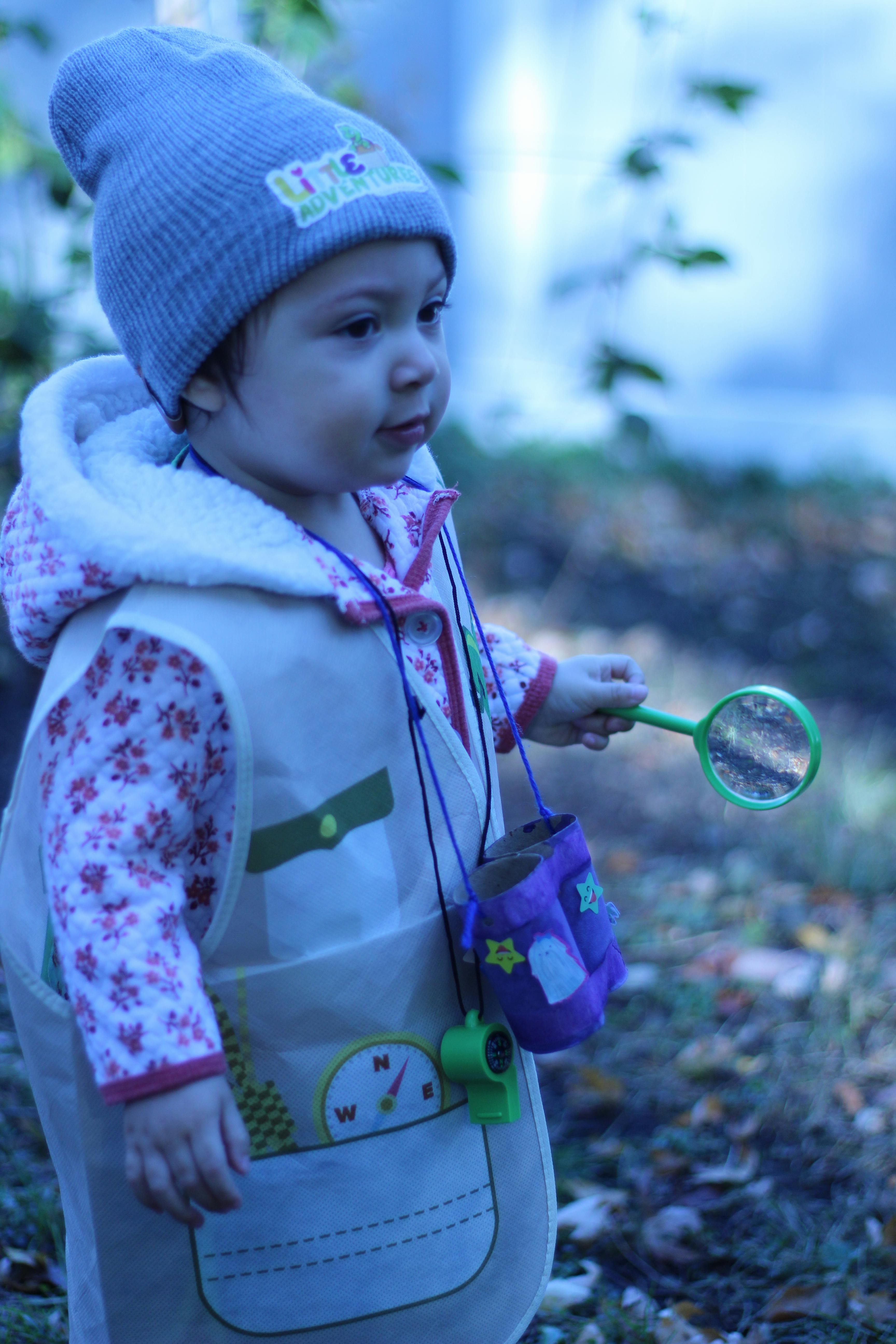 Child in a beanie and vest holding a magnifying glass