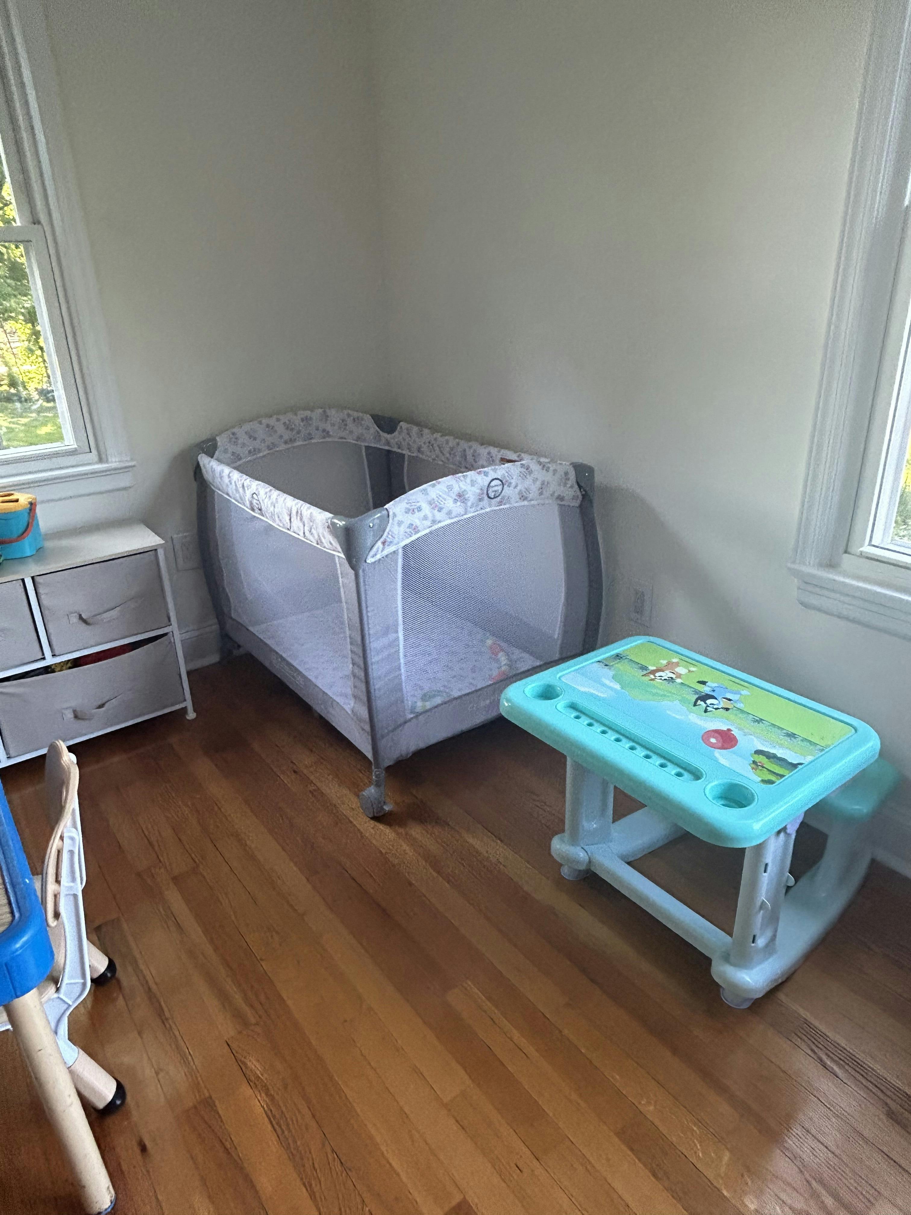 Baby playpen and child's desk in a room with hardwood floors
