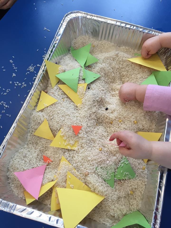 Child's hands playing with rice and paper triangles in a tray
