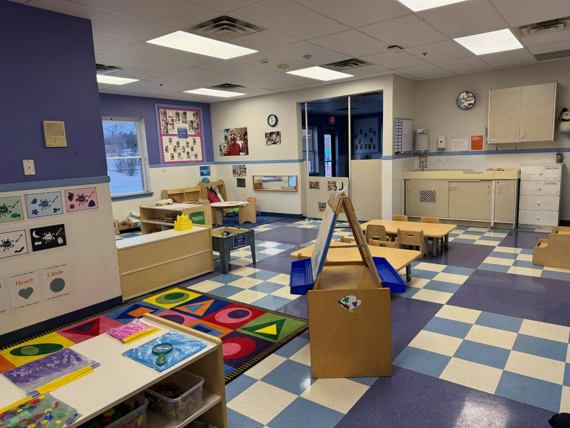 An empty early childhood classroom with colorful rug, tables, and art supplies