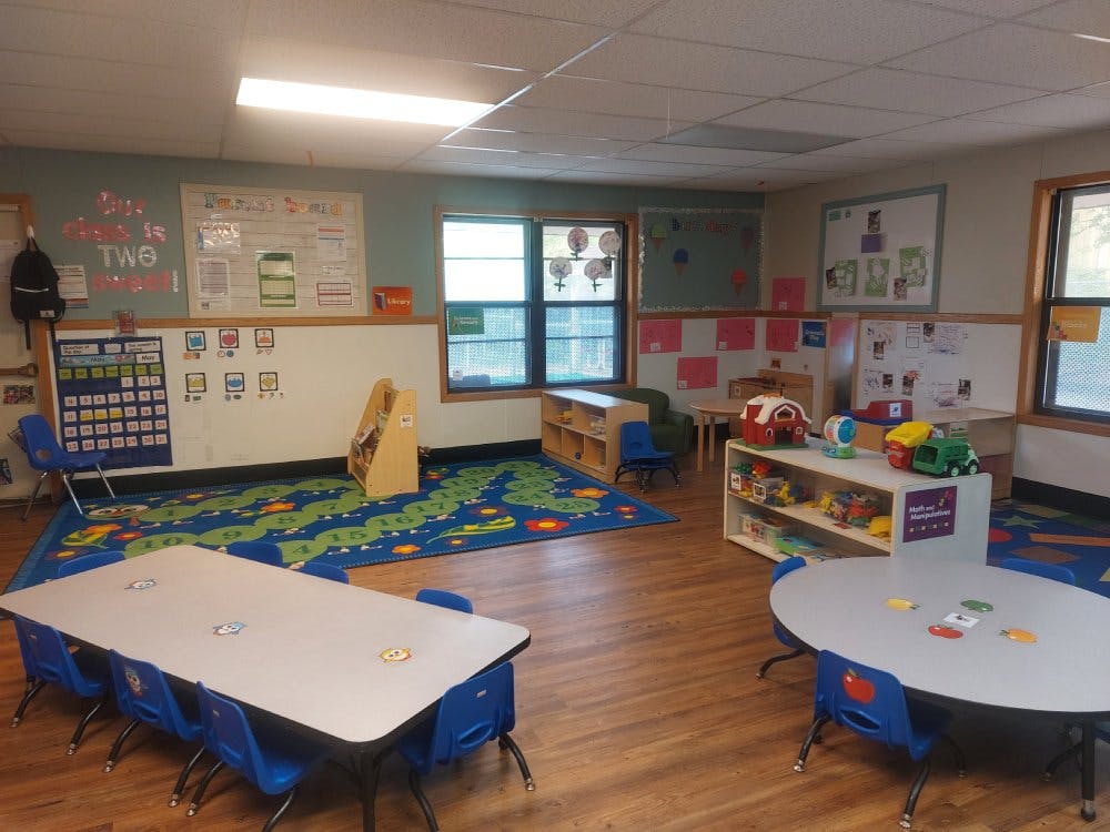 Classroom with small tables and chairs, a play area, and learning materials