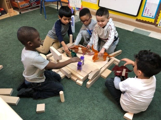 Five children playing with wooden blocks and toy animals on a green carpet