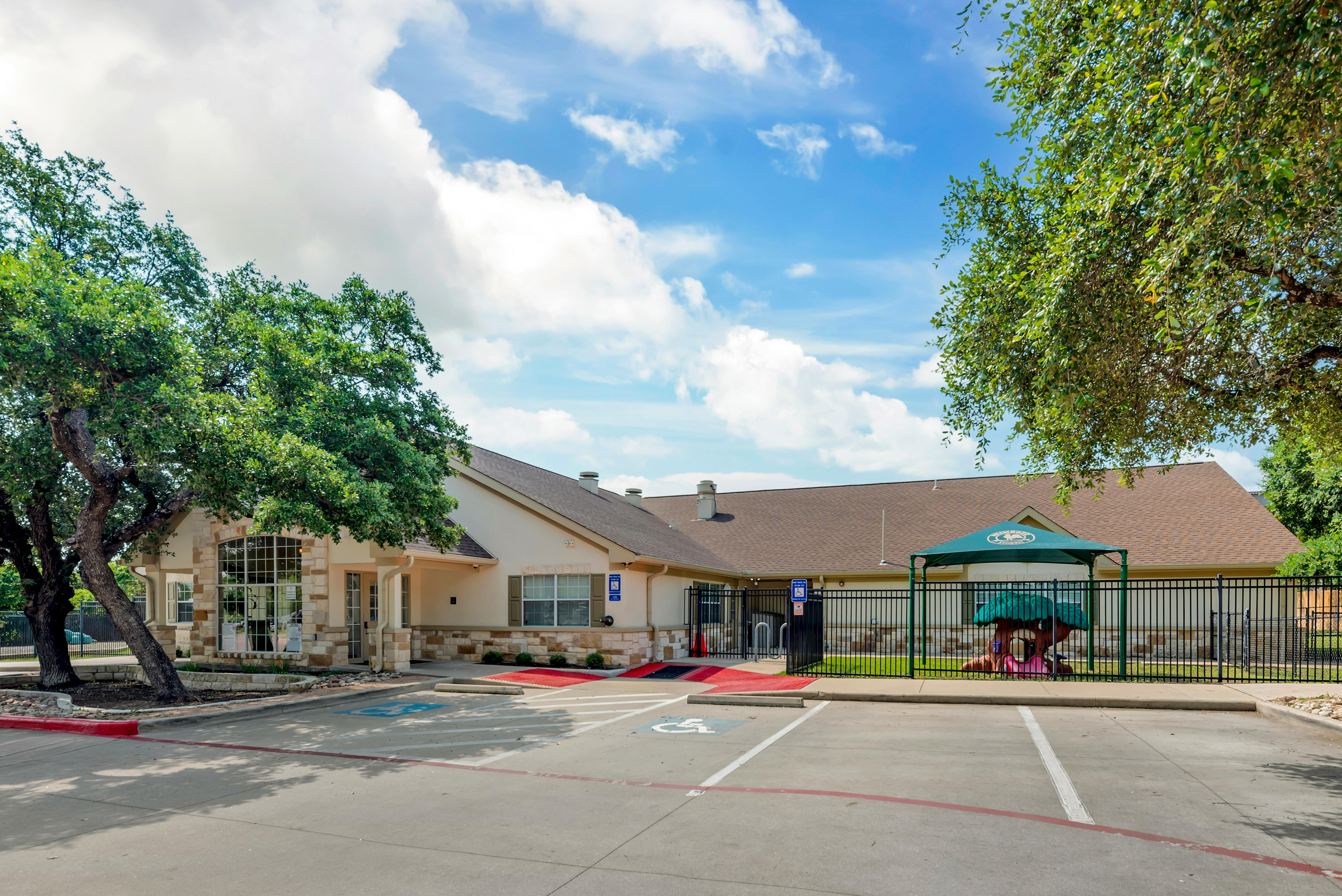 Building exterior with a parking lot and a fenced play area with a green canopy