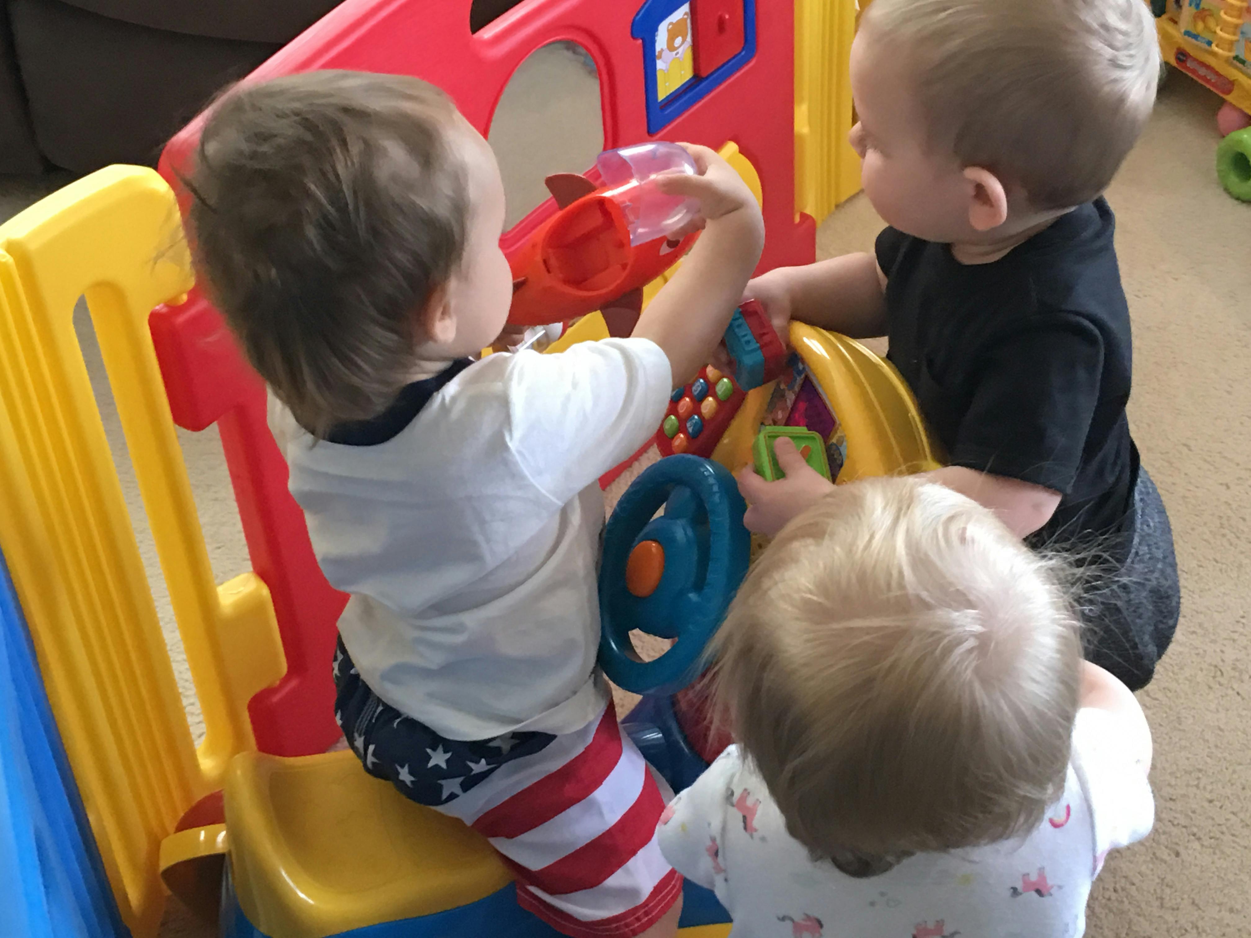 Three children playing with a colorful activity toy