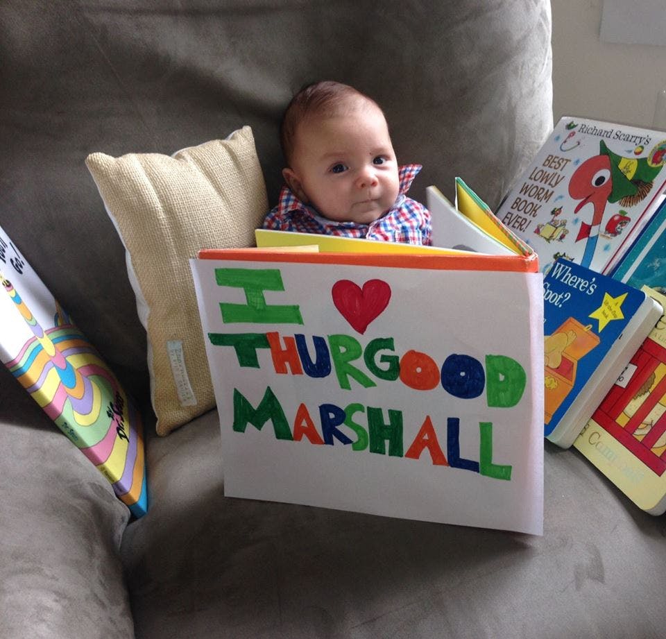 Baby sitting behind a book that says "I love Thurgood Marshall"