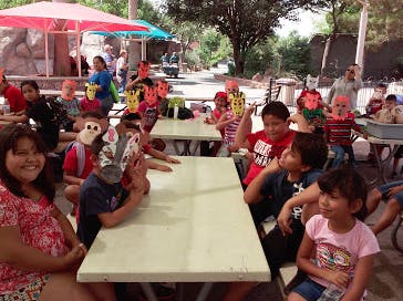 People and children sitting at tables outdoors, some wearing animal masks