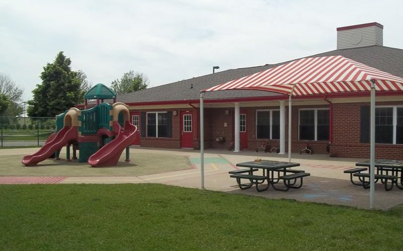 Playground with slides next to a brick building and covered picnic tables