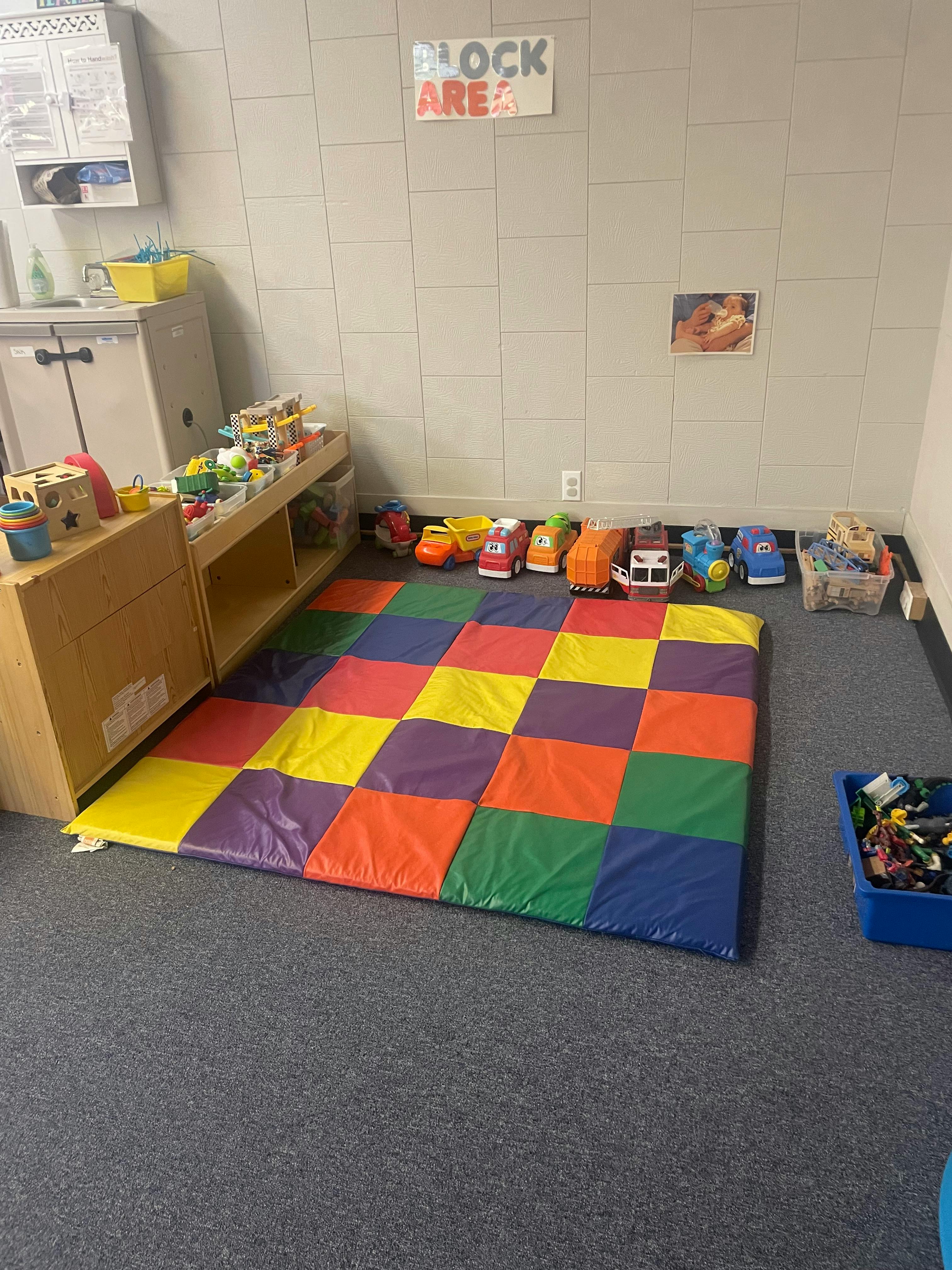 Playroom with colorful mat, toy cars, and shelves with "BLOCK AREA" sign